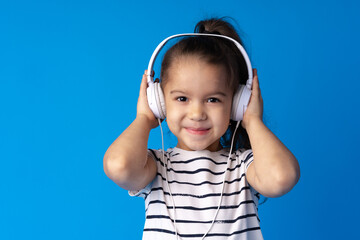 Little girl child wear headphones listen to music over blue background