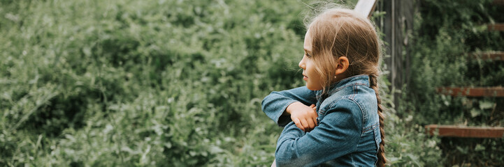 thoughtful candid eight year old kid girl stands on staircase with grass and enjoying nature. prepubertal age of children and their lives, mind psychology and mental health concept. banner. mockup