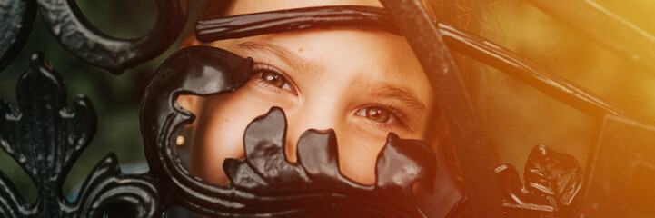 portrait happy candid eight year old caucasian kid girl brown eyes peeking through of abstract metal shapes in nature. prepubertal age of children, mind psychology and mental health. banner. flare