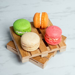 Sweet and colourful macaroons served on little wooden pallets on a marble texture table. Traditional french dessert.