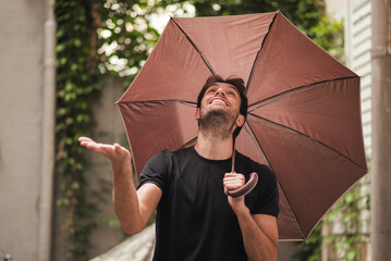 Young handsome man holding his umbrella, looking up to the sky and checking the weather, smiling