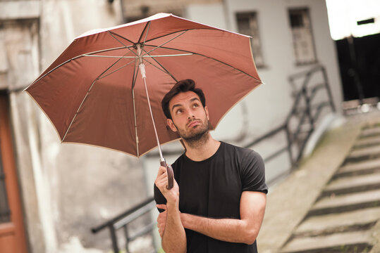 Young handsome man holding his umbrella, checking the weather, looking up to the sky