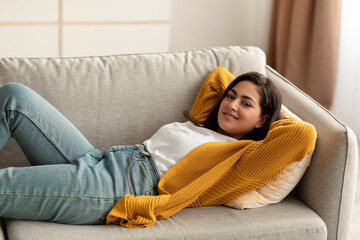 Total relax. Happy arab woman lying with hands behind head on comfortable sofa and smiling, having great day off