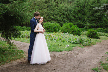 the groom hugs the bride from behind against the background of spruce, they smile and look at each other with love