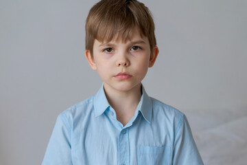 A small caucasian boy in casual blue shirt looks into camera with serious look, natural expression. Confident look straight with brown eyes