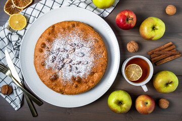 Close-up top view of an apple pie surrounded by fresh ripe apples. Homemade cakes with seasonal fruits, DIY. Selective focus.