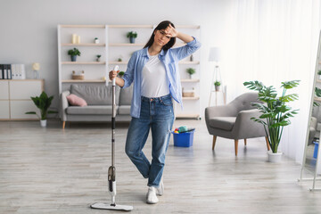 Tired woman cleaning floor with mop in living room