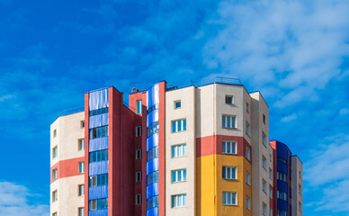 Fototapeta premium Modern multi-storey building with multi-colored facade against blue cloudy clear sky.