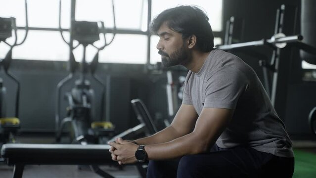 Young Indian athlete thinking or resting at gym after wrokout - Concept of thoughtful, relaxation and fitness center.
