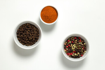 Spices assorted colorful peppercorns and powder paprika in bowls on white background.