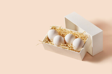 White organic eggs in a box with straw on a pastel peach background. Copy space