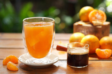 A glass of orange juice served with black coffee decorated with oranges on wood table on nature background.