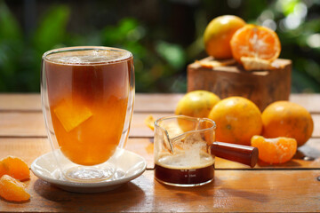 A glass of orange juice served with black coffee decorated with oranges on wood table on nature background.
