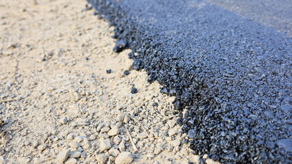 Close-up of the new asphalt curb. On the edge of a new paved road with soil and stone material with copy space. Selective focus