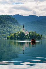Romantic young couple rowing a boat on lake Bled in Slovenia with church on island and hills in background