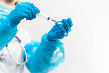 Young woman doctor in a medical mask and gloves with a syringe in her hand and a stethoscope in a hospital during a coronavirus pandemic. Selective focus. Portrait