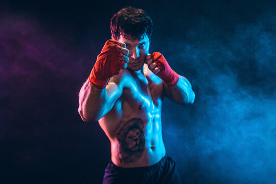 Portrait of muscular kickbox or muay thai fighter who punching on smoke background. Sport concept.