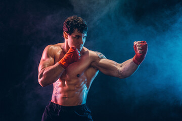 Side view of muscular shirtless boxer who preparing for fight on smoke background. Sport concept