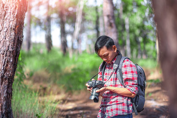 Young man holding a camera and looking a pictures while standing at the forest. Environmental studies.