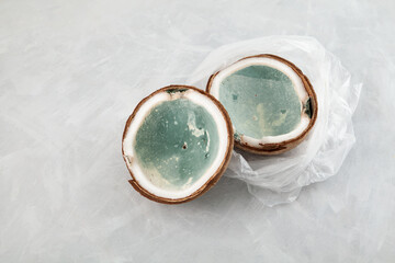 Moldy spoiled coconut in plastic bag on light grey surface. Improper food storage. Reduction of organic waste