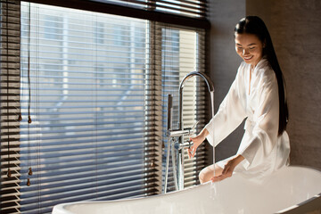 Happy attractive chinese lady sitting on bath, copy space