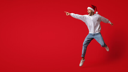 Look There. Excited Young Man In Santa Hat Jumping And Pointing Aside