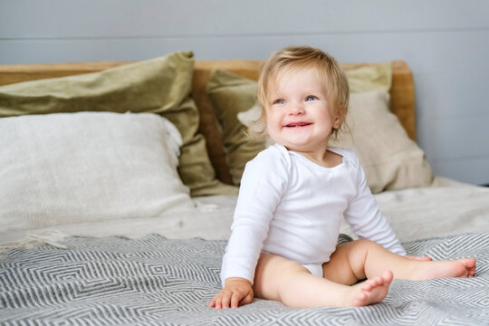 Baby in white clothes sits on the bed and laughs. High quality photo