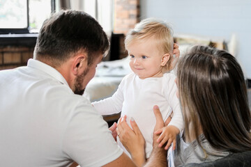 Fototapeta premium Young parents sit on the couch and hug the baby. High quality photo