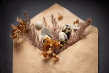 Happy easter composition with small eggs and dried flowers in craft paper envelope