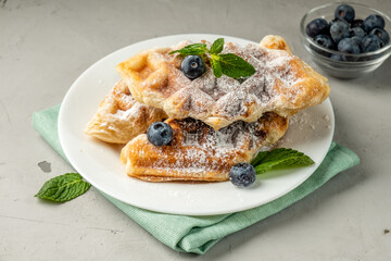 Croissant and waffles in one Croffles sprinkled with powdered sugar and garnished with blueberries and mint leaves.