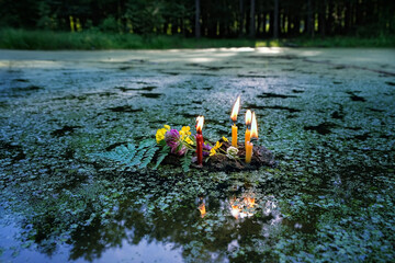 flowers and burning candles on dark water, covered aquatic plants duckweeds (Lemna). old tradition, fortune telling for pagan holiday. Summer Solstice Day, Midsummer, wicca, Litha sabbat - obrazy, fototapety, plakaty