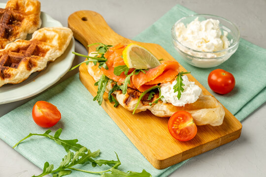 Croffles with fish and soft cheese on a wooden board and light background.