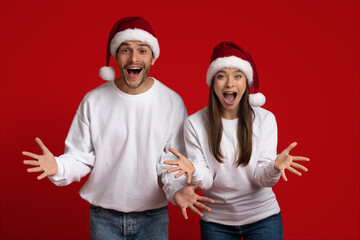 Amazing Sales. Emotional Young Couple In Santa Hats Spreading Hands With Excitement