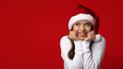 Christmas Wish. Dreamy Young Woman In Santa Hat Touching Face In Excitement