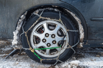 Snow chains on a car wheel. The fenders of the car are forgotten by the muddy snow. The concept of...