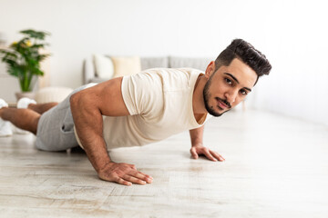 Fototapeta na wymiar Attractive young Arab man standing in plank pose or doing push ups on mat at home