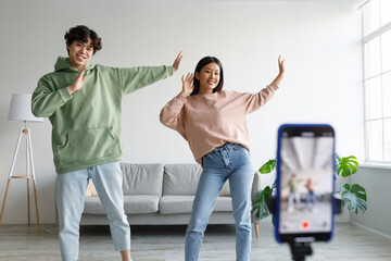 Young Asian couple recording video content, dancing on smartphone camera at home. Vlogging concept