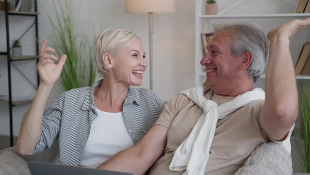 Winner excitement. Happy couple. Common interests. Joyful middle-aged man and woman looking laptop feeling euphoric of results competition sitting light home interior.