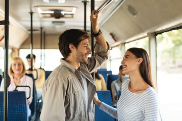 Cheerful young couple standing in bus and talking