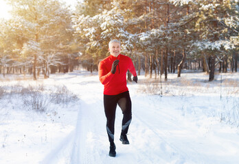Cold weather running. Full length portrait of mature man in sportswear jogging at snowy winter...