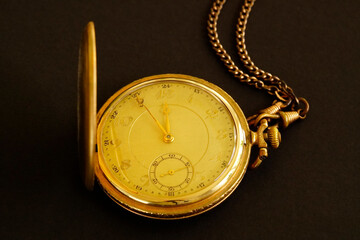 Old gold plated pocket watch against a black background.
