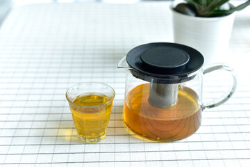 Cup of tea and glass jars on the table covered with white cloth. Hot Tea  water is poured from the kettle into a cup with tea leaves. Pour black tea into a glass cup on table in cafe. selected focus