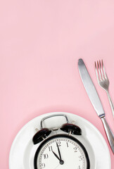 Concept of intermittent fasting, ketogenic diet, weight loss. fork and knife, alarmclock on plate
