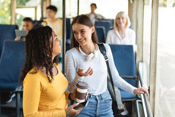 Beautiful multiethnic smiling women standing in bus and talking © Prostock-studio