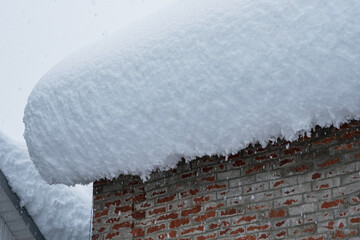 The red brick wall of the house and the huge snowdrift on the roof. In the background is a gray sky with large flakes of falling snow. The aftermath of the snow storm.
