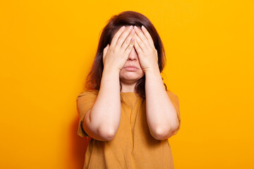 Stressed adult covering face and eyes with palms. Woman standing with hands on closed eyes, feeling emotional over isolated background. Shy person hiding facial expression from camera