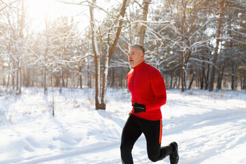 Athletic senior man in sportswear running at winter park, jogging outdoors on frosty sunny morning,...