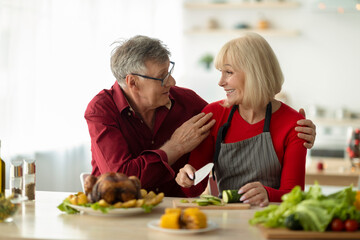 Loving senior couple looking at each other while preparing traditional roasted turkey for Christmas dinner at home