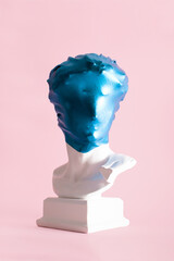 Plaster male head wrapped in shinny blue stretch fabric against pastel pink background. Blue in the...