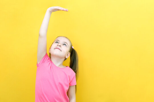 Little cute girl measuring her height on a yellow isolated background.